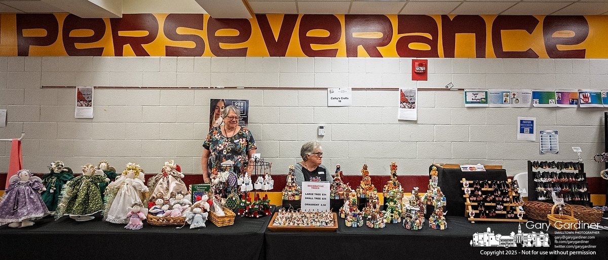 Two women sell handmade dolls and decorative trees in the main hallway by the student lockers at Westerville North High School during the Mark Twain Craft Bazaar. Above them, a banner reading "Perseverance," one of the school’s core values, underscores the spirit behind their