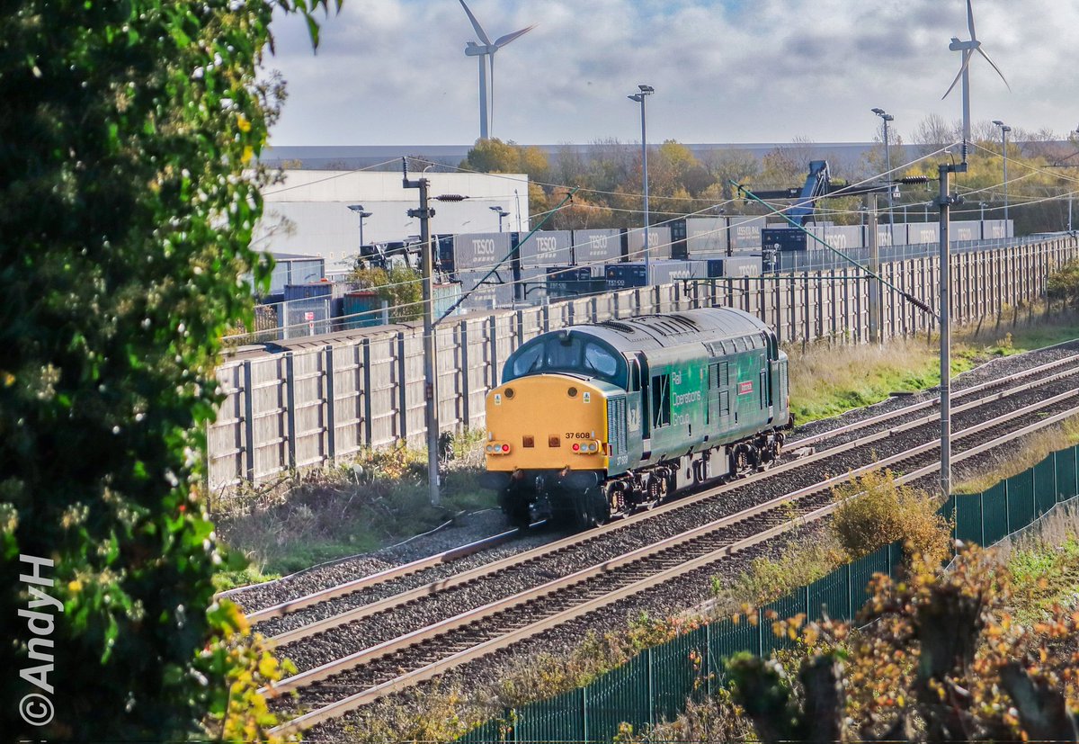 holtona72's tweet photo. #SyphonSunday @RailOpsGroup 37608 'Andromeda' heads away from the camera, past the windmills & Tesco containers at #DIRFT & south towards Northampton, from where it was collecting a #Class350 EMU to take to Derby.
0M99 Derby RTC to Northampton EMD.
@TheGrowlerGroup #ROG 1/11/25 https://t.co/GqeNJbtsr9