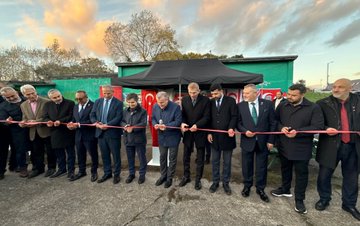 First image shows a man in a suit speaking into a microphone at a podium under a black canopy with Turkish flags banners and posters of Turkish figures and federation logos on a green background. Second image depicts two men one in a black coat and one in a blue jacket standing on a grassy soccer field with a ball at their feet surrounded by autumn trees and a crowd in the background. Third image captures a group of men in formal attire and sports jerseys shaking hands and holding medals under a canopy with Turkish flags and event banners. Fourth image features a line of men in suits cutting a red ribbon in front of a structure with Turkish flags on a paved area during sunset with trees nearby.