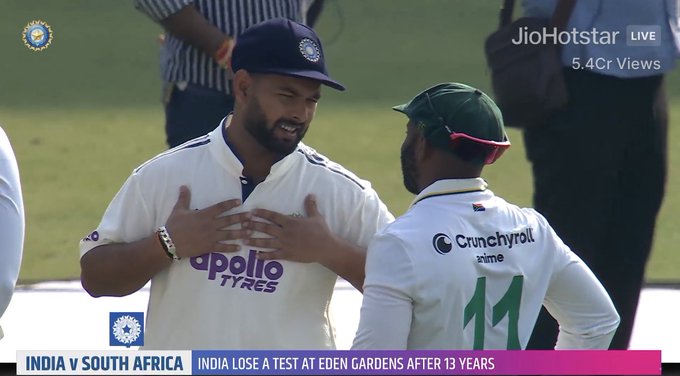 Rishabh Pant wears white India cricket uniform with Apollo Tyres sponsor on sleeve and wristband, gesturing with hands while facing Temba Bavuma in green South Africa cap and jersey. Background includes cricket field grass, other players in white uniforms numbered 11 and 13 with Crunches logo, Jio Hotstar live broadcast watermark, and text overlay South Africa India Test at Eden Gardens noting India lose a Test at Eden Gardens after 13 years.