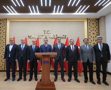 First image shows five men in suits standing on steps in front of a building with gold sign reading Malatya Valiligi, flanked by columns; two children, a boy in white shirt with red and white vest and a girl in colorful embroidered dress holding red flowers, stand in front smiling. Second image depicts ten men in suits standing behind a wooden podium with MNE logo under Turkish flags in a room with gold ornate walls and ceiling lights. Third image features twelve men in suits seated around a wooden table with water bottles in an elegant room with chandelier, wooden walls, portraits of Mustafa Kemal Ataturk, and Turkish and another flag.