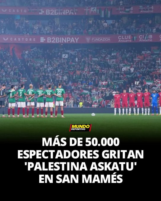 A vibrant stadium filled with thousands of fans waving green flags and scarves under stadium lights, with advertising banners for brands like BBVA and Castore visible on the perimeter. In the foreground on the green field, a line of male soccer players in green jerseys with numbers like 23 and 22 stand facing the crowd, some with hands on hips. Opposite them, players in red and white striped jerseys and blue kits are positioned, all appearing attentive to the stands. Overlaid yellow text reads MAS DE 50.000 ESPECTADORES GRITAN PALESTINA ASKATU EN SAN MAMES.