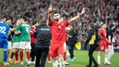 First image shows San Mames stadium at night illuminated in red and white stripes with a large screen displaying text, surrounded by crowds and lights. Second image depicts two teams of soccer players in green and red jerseys lined up on the field before a match, with a flag in the air and packed stands behind. Third image captures a player in a red Palestine jersey number 4 raising both arms in victory pose on the green field, surrounded by teammates and officials in various uniforms. Fourth image presents a wide night view of a full circular stadium packed with spectators, bright lights illuminating the green soccer field and surrounding areas.