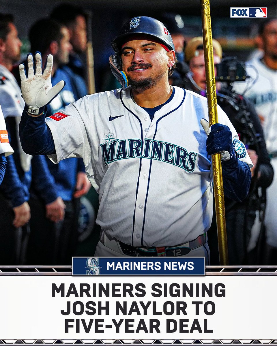 Josh Naylor stands on a baseball field wearing a white and navy Seattle Mariners uniform with number 22, holding a gold flagpole in his right hand and raising his left hand in a wave, smiling with a mustache, surrounded by blurred team staff and FOX Sports camera equipment, overlaid with text Mariners News, Mariners Signing Josh Naylor to Five-Year Deal.