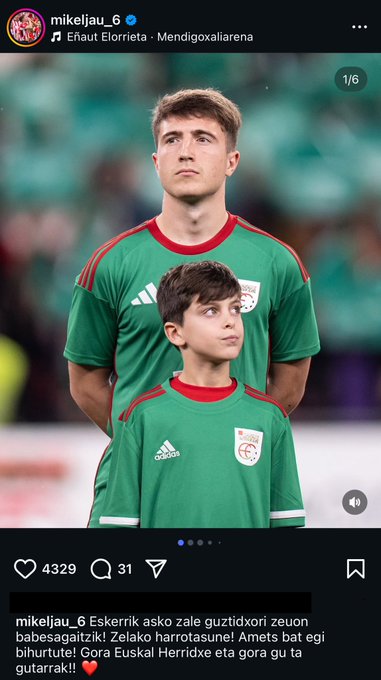 Two males stand side by side in a stadium setting wearing matching green jerseys with red accents and the Euskal Selekzioa logo, the taller one with short brown hair looking upward and the shorter one with curly dark hair looking forward, both in athletic pose with arms at sides.