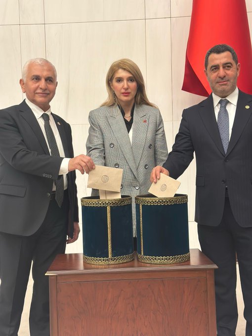 First image shows three adults in formal suits standing at a wooden table with two ornate velvet-covered ballot boxes one holding envelopes; a Turkish flag hangs in the background against a light wall in a formal setting. Second image depicts a woman in a gray suit with a pin sitting at an orange-seated desk in a large chamber filled with similar orange chairs and desks some occupied by other suited individuals in the background.