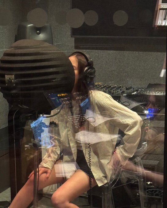 Woman with long dark hair wearing glasses and gray sweater sits on camouflage-patterned couch holding red-cased smartphone. Man with headphones sits in checkered chair in brick-walled studio with white wall, microphone stands, speakers, turntable, and window showing trees. Woman with long hair wearing headphones and striped shirt with shorts stands in dark room with foam panels, mixing console, and equipment.