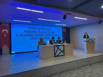 First image shows a man in a suit standing at a wooden podium speaking into a microphone with a blue screen behind displaying Turk Buro Sen and Ankara IS-KUR Sube 2.Olagan Hos Genel Kurultay text, Turkish flags on sides, several men in suits seated at a table with documents, another man standing nearby, modern conference room with lighting and banners. Second image depicts a large group of about 20-30 people mostly men and some women in formal suits standing in rows in a spacious hall with red chairs, Turkish flags and other banners on walls, wooden tables in front, neutral lighting. Third image features a woman in a suit speaking at the podium with microphone, blue screen showing Turk Buro Sen and event title, men seated at table including one with glasses, Turkish flags, wooden table with X logo, conference setup. Fourth image shows three men in suits seated at a wooden table with documents and water glasses, blue screen with Turk Buro Sen and Ankara IS-KUR Sube 2.Olagan Hos Genel Kurultay, Turkish flags, modern room with lighting.
