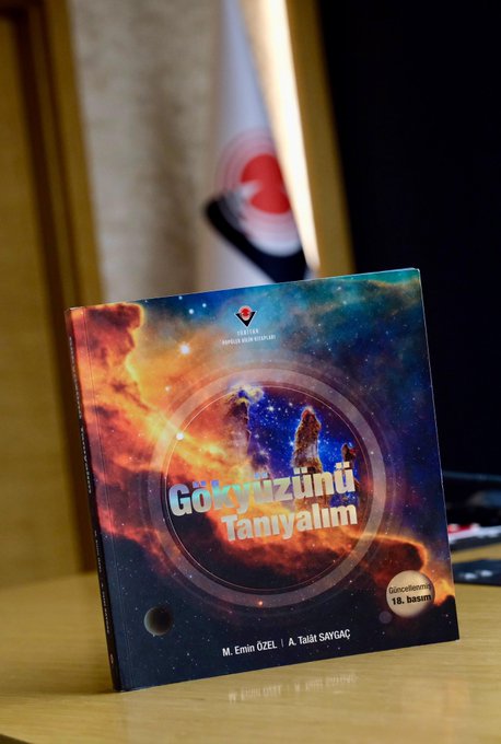 A large full moon glows orange against a twilight sky above rugged brown hills covered in sparse vegetation. Below the hills, a cluster of white multi-story apartment buildings with red-tiled roofs lines the base, some illuminated by warm lights. The scene captures the Super Moon in its closest approach to Earth, appearing larger and brighter than usual. Another similar image shows the pinkish moon rising over the same landscape with buildings. A book cover displays a cosmic scene with stars and galaxies in orange and blue hues, titled Gökyüzünü Tanıyalım by M. Emin Özsah, published by TÜBİTAK. An open book page features diagrams of the moon with craters, phases, and textual explanations in Turkish about lunar features and exploration.