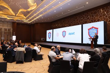 First image displays a young girl in a blue shirt standing on green grass with arms raised happily in front of a school building under a blue sky with bubbles, featuring Turkish flag shield emblem labeled Tertemiz Yarışması Sosyal Sorumluluk Yarışması Başlıyor with text on cleaning and hygiene project details, Son Başvuru 10 Kasım 2023, QR code, and logos of MEB and OPET. Second image shows a large group of adults in business attire standing together on a patterned floor in a conference hall with decorative walls and screens displaying Turkish flags, OPET logo, and event branding. Third image depicts a woman in orange top and black pants speaking at a podium in a modern room with wooden walls, hanging lights, multiple screens showing project visuals, and audience seated at round tables with drinks and notebooks. Fourth image illustrates a man in suit speaking at a podium in a similar conference setting with wooden decor, screens displaying shields and OPET logo, audience at tables including diverse group of men and women in formal wear.