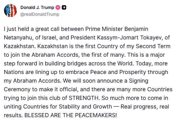 Photograph displays Israeli Prime Minister Benjamin Netanyahu positioned in the center wearing a dark suit and tie, with former US President Donald Trump on his right in a blue suit and red tie smiling and gesturing with one hand, and Kazakhstans President Kassym-Jomart Tokayev on his left in a black suit looking forward, all standing closely together in a formal indoor setting with a blurred background of ornate decor and flags.