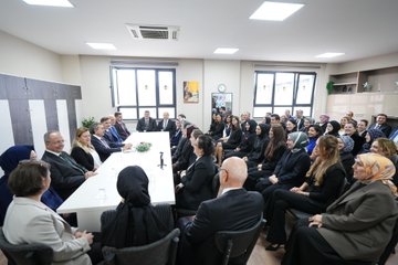 First image shows a family including a man in a suit, a woman in black attire, and two young children in orange school uniforms with backpacks standing at the entrance of Can Gür İlkokulu school building decorated with red balloons and flowers. Second image depicts officials including a man in a blue suit and a woman in orange at a signing table with microphones, Turkish flags, and portraits of Mustafa Kemal Atatürk and Recep Tayyip Erdoğan in the background during a protocol event. Third image features a large group of suited men and women, some in headscarves, with two children in orange uniforms posing on a stage with green banners reading T.C. Millî Eğitim Bakanlığı and TOGEM-DER. Fourth image shows numerous people seated around a white table in a meeting room with windows, plants, and a clock, including women in various attire like headscarves and suits, engaged in discussion.