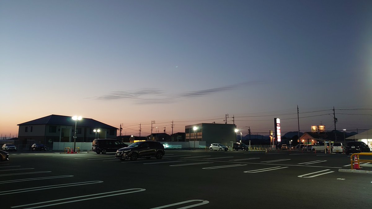 PCM8's tweet image. 夕暮れの駐車場、アスファルトに夜の気配がしみこんでいく。
空の端っこには淡いグラデーション、
群青とオレンジのあいだに、さざ波みたいな雲が浮かんでいた。

エンジン音も遠く、街灯の灯りがひとつ、またひとつ。
静かな帰り道に、今日の記憶がゆっくり冷めていく感じ。…
