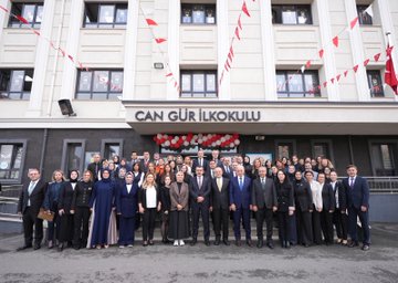 First image shows four adults and two children seated at a table with microphones during a formal event with Turkish flags and banners reading Millî Eğitim Bakanlığı and TOGEMDER on a screen behind them including portraits of officials and event title about photography education protocol in Istanbul. Second image depicts three adults and two children standing together holding red certificates with TOGEMDER and ministry logos on a screen in the background at the same event. Third image captures a large group of about 18 adults and two children in formal attire posing on a stage with ministry and TOGEMDER banners below a screen showing Turkish flags. Fourth image features a large group of adults in professional clothing standing in front of Can Gür İlkokulu building entrance decorated with Turkish flags and balloons.