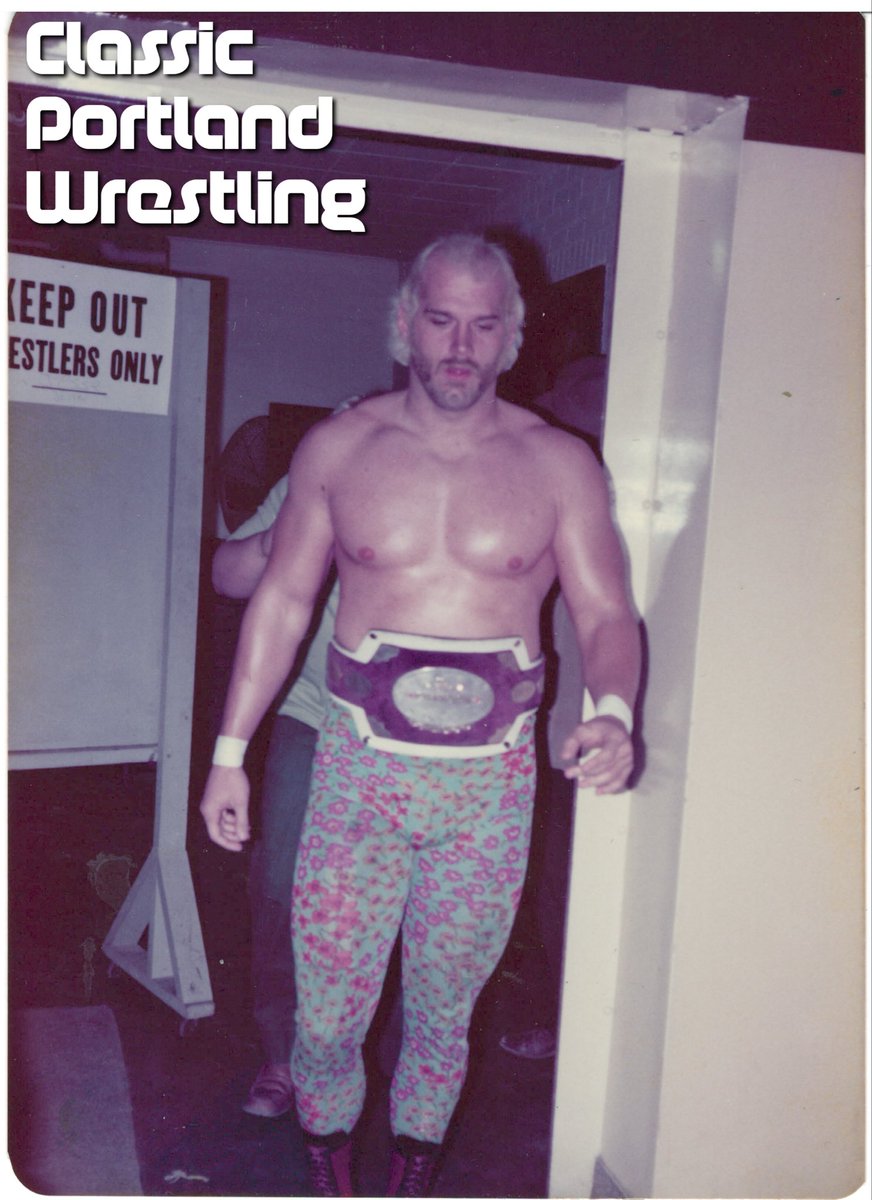 Jesse “The Great One” Ventura with the Pacific Northwest Heavyweight title belt photographed leaving the dressing room area at the JM Perry institute in Yakima, WA. While obscured by Ventura, Rose is following close behind. This photo was taken by Merlin Vickerman in Fall of ‘76