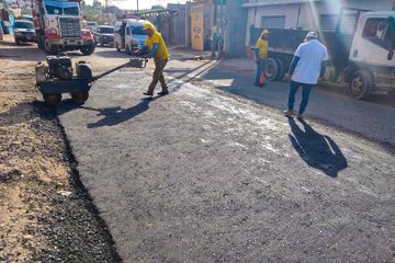 First image shows three workers in yellow vests and helmets using shovels and a machine to break up damaged asphalt on a street with trucks and buildings nearby. Second image depicts four workers in yellow safety gear spreading and leveling fresh asphalt on a road using rakes near vehicles and traffic cones. Third image features workers operating a roller machine on newly paved asphalt beside parked trucks and construction barriers. Fourth image illustrates workers in vests applying final touches to a smooth asphalt road surface with cones and vehicles in the background.