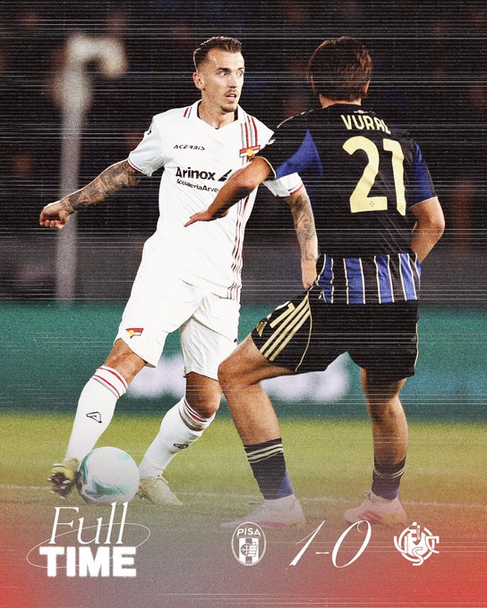 Two soccer players in action on a green field during a match one in white and red Cremonese jersey with tattoos on arms dribbling a white soccer ball while the other in blue and black Pisa jersey number 21 marked VURNI defends nearby both wearing matching shorts and socks with sponsor logos visible on jerseys and the score overlay shows FULL TIME Pisa 1-0 Cremonese