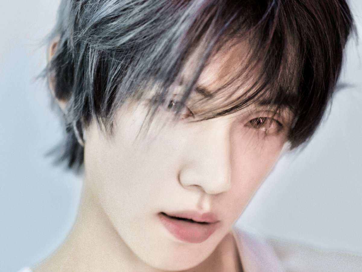 Close-up portrait of a young man with short silver-gray hair featuring bangs, fair skin, almond-shaped eyes with a soft gaze, straight nose, and slightly parted lips in a neutral expression, set against a light blue background with subtle color gradients.