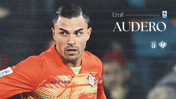 Emil Audero wearing an orange and gray Cremonese soccer jersey with sponsor logos stands on the field looking focused during a match with stadium background and text overlay Emil Audero above the image.