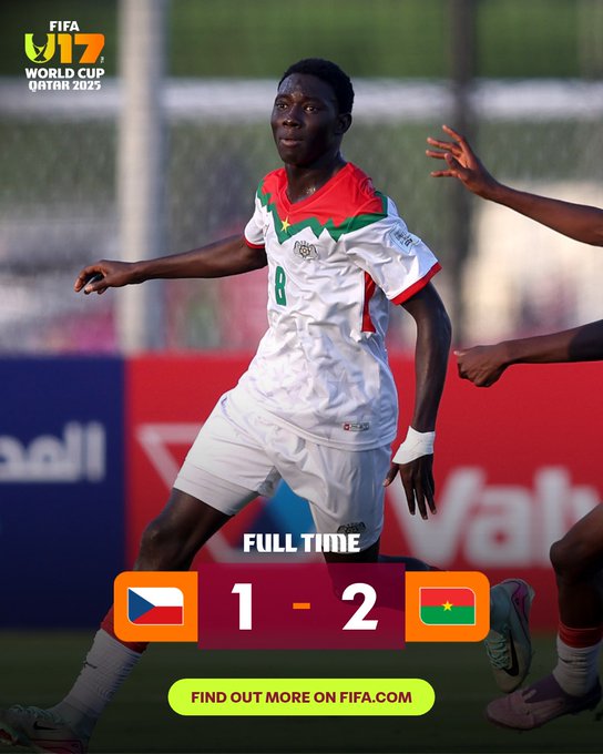 A soccer player from Burkina Faso wearing a white jersey with green and red accents and number 8 stands on the field with arms outstretched in celebration as teammates touch his shoulders. The background shows a stadium with red barriers and Arabic text signage. FIFA U-17 World Cup Qatar 2023 logo appears at the top. Scoreboard displays full time Czech Republic 1 - 2 Burkina Faso with flags. Green find out more on fifa.com text at bottom.
