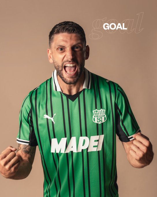 A man with short dark hair and a beard wearing a green and black striped soccer jersey with PUMA logo, Mapei sponsor text, and U.S. Sassuolo club emblem on the chest, stands against a beige background, mouth open in a celebratory yell, arms raised with hands open, and the word GOAL overlaid in white text.