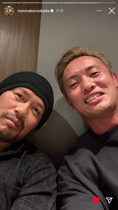 Two men sitting on the floor leaning against a light wooden wall one with short dark hair wearing a black beanie and gray patterned shirt the other with blond hair in a black hoodie both smiling at the camera with teeth visible casual indoor setting Instagram watermark in top left corner
