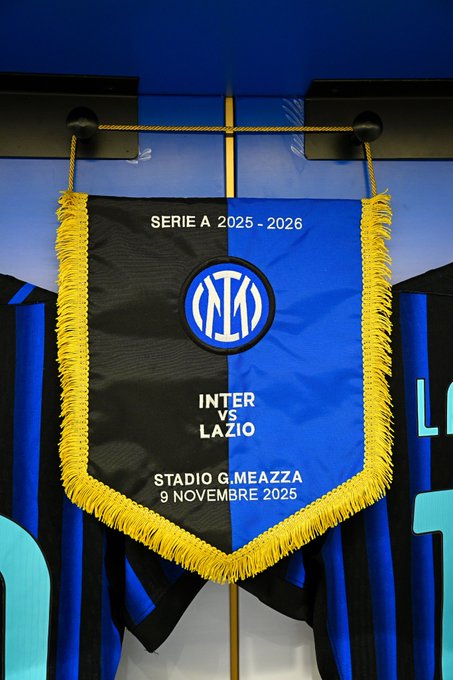 A vertical banner hangs in a stadium setting with blue and black Inter Milan team jerseys displayed below it. The banner has a black background with blue and gold fringes and features the Serie A logo at the top. Below it shows the Inter Milan club logo followed by text reading INTER LAZIO. At the bottom it states STADIO MEZZA 9 NOVEMBRE 2025 indicating the match details.