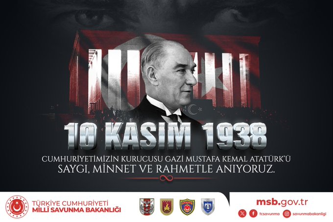 A formal portrait of Gazi Mustafa Kemal Atatürk in a suit and tie centered against a dark background with red vertical stripes resembling the Turkish flag on either side the text 10 KASIM 1938 in silver lettering above him and below it in white text CUMHURİYETİMİZİN KURUCUSU GAZİ MUSTAFA KEMAL ATATÜRK with the Ministry of National Defence logo and emblem at the bottom right