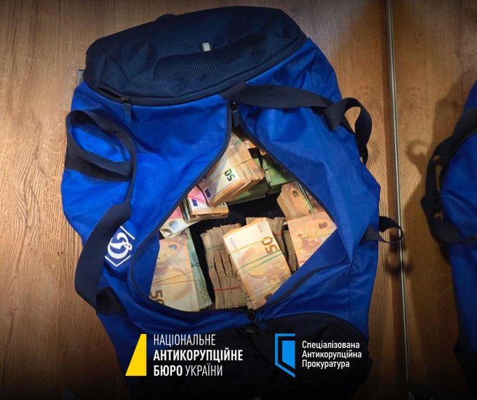 First image shows stacks of US dollar bills bundled with Federal Reserve bands labeled with serial numbers like ANTA00096058 and KAN CITY000417A on a desk in an office with bookshelves and a computer monitor in the background, alongside NABU and Anti-Corruption Prosecutorate logos. Second image depicts a blue backpack open on a wooden floor with mirrors reflecting it, containing bundles of Ukrainian hryvnia banknotes, and NABU and Anti-Corruption Prosecutorate logos visible. Third image displays a luxurious bathroom interior with gold-colored walls patterned with ornate designs, two gold toilets, sinks with gold faucets, a chandelier, and decorative elements like a rug and tissue holder. Fourth image portrays a middle-aged man with a beard wearing a blue suit and white shirt, seated at a formal event with other men in suits, flowers on the table, and a number 20 visible.