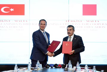 First image shows two men in dark suits standing side by side in front of a light gray wall with the emblem of the Turkish Ministry of National Education centered, flanked by two Turkish flags on stands. The man on the left has short dark hair and wears a blue tie, while the man on the right has glasses and a gray tie. The floor is blue carpet with a modern interior setting. Second image depicts two men in suits shaking hands over a table with water bottles and documents, holding red-bound agreements labeled Turkiye Malta in white text on screens behind them showing Turkish and Maltese flags. The setting is a formal conference room. Third image features a group of six people seated in an ornate room with sofas and a wooden table, including men in suits and a woman in a headscarf, with Turkish and another flag, a painting of children on the wall, and patterned carpet.