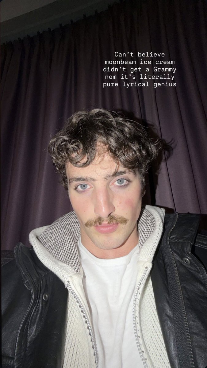 Benson Boone aparece em uma sala pouco iluminada com luz roxa, vestindo um moletom branco por baixo de uma jaqueta de couro preta, com cabelo cacheado, bigode e olhar direto para a câmera, com um texto sobreposto que diz: "Não acredito que o sorvete Moonbeam não foi indicado ao Grammy, é pura genialidade lírica."