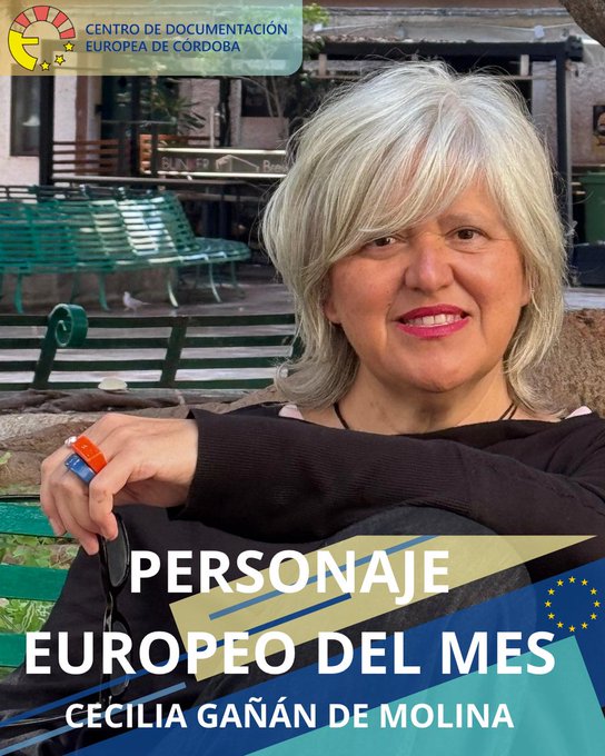 A woman with blonde hair wearing a black top and colorful ring sits on a green bench outdoors near green benches and a building with the text Centro de Documentación Europea de Córdoba at the top and below it Personaje Europeo del Mes Cecilia Gañán de Molina with EU flag symbols