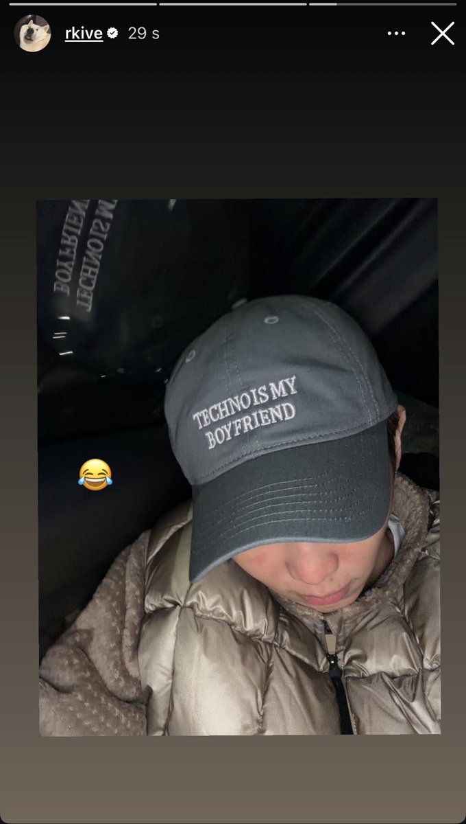 A gray baseball cap with white embroidered text reading Techno Boyfriend rests on a surface inside a car, next to a black backpack or bag. The cap has a curved brim and is positioned in a dimly lit interior with beige padded seats visible in the background. An Instagram story interface overlay includes the username rkive and a timestamp of 29s.