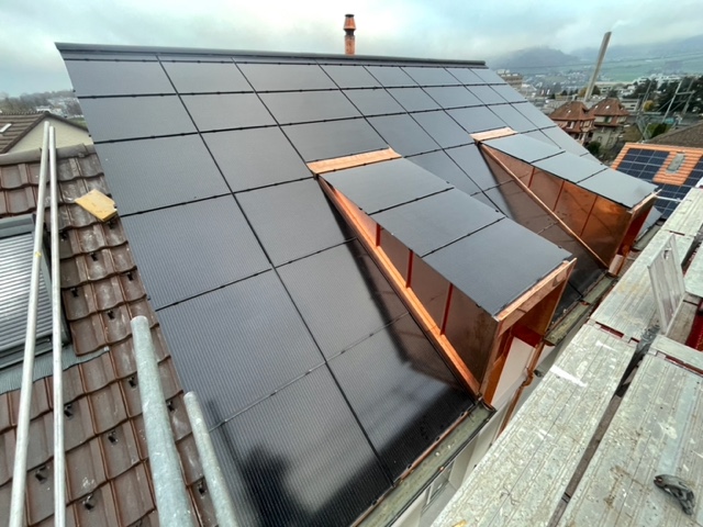 Haus von 1950 erhöht seinen Wohnraum um 50% und senkt seinen Energiebedarf um 92% nach der energetischen Sanierung.
Die Ölheizung wurde durch eine effiziente Wärmepumpe ersetzt. Der neue Dachstock aus Holz bindet 20 t CO₂.  
Dank 13,3 kW PV-Anlage ist es ein Plusenergiehaus.