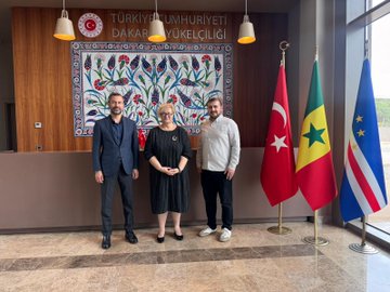 First image shows a stage with banners for 12ème Congrès Confédération Nationale des Syndicats du Sénégal CNTS theme Les défis du travail et la migration on November 8 and 9 2025 at Grand Théâtre speakers at podium with microphones chairs and flags. Second image depicts a large audience in an auditorium many wearing red attire seated attentively in rows with wooden floors and red seats. Third image features three people standing in a modern office with Turkish and Senegalese flags decorative wall art and Turkish Republic Dakar Embassy sign two men in suits and one woman in black dress. Fourth image displays stage setup similar to first with speaker at podium raising fist banners for CNTS congress theme and participants seated nearby.