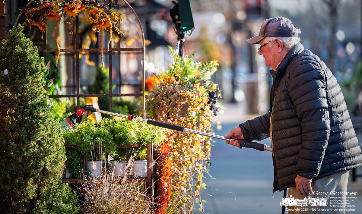 Dave Talbott waters the last of the season’s perennials arranged in baskets and trays outside his florist shop on North State Street. My Final Photo for November 14, 2025.  rebrand.ly/mfp111425