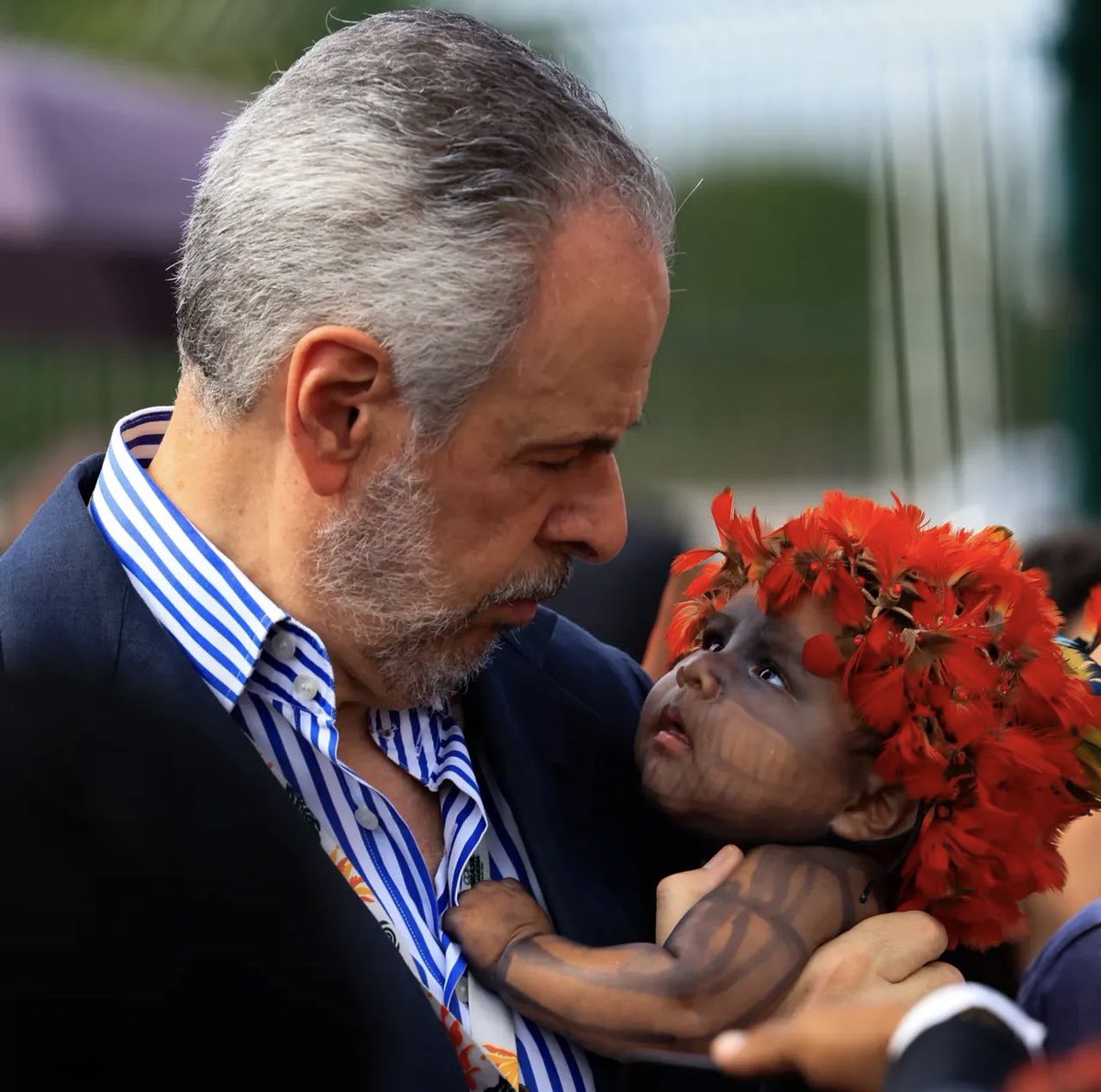 MarceloBacana's tweet photo. Cena da COP
O presidente da conferência André Corrêa do Lago, protagonizou um daqueles momentos que viram símbolo: no colo, um bebê indígena, olhos atentos, cocar vermelho vivo — pura Amazônia.
A foto, clicada por Wilton Junior, do Estadão, correu mesas e celulares. No auge da tensão para liberar a entrada da conferência, a imagem acabou dizendo mais do que qualquer discurso: no fim das contas, é por essas pequenas grandes vidas que todo mundo ali está brigando.