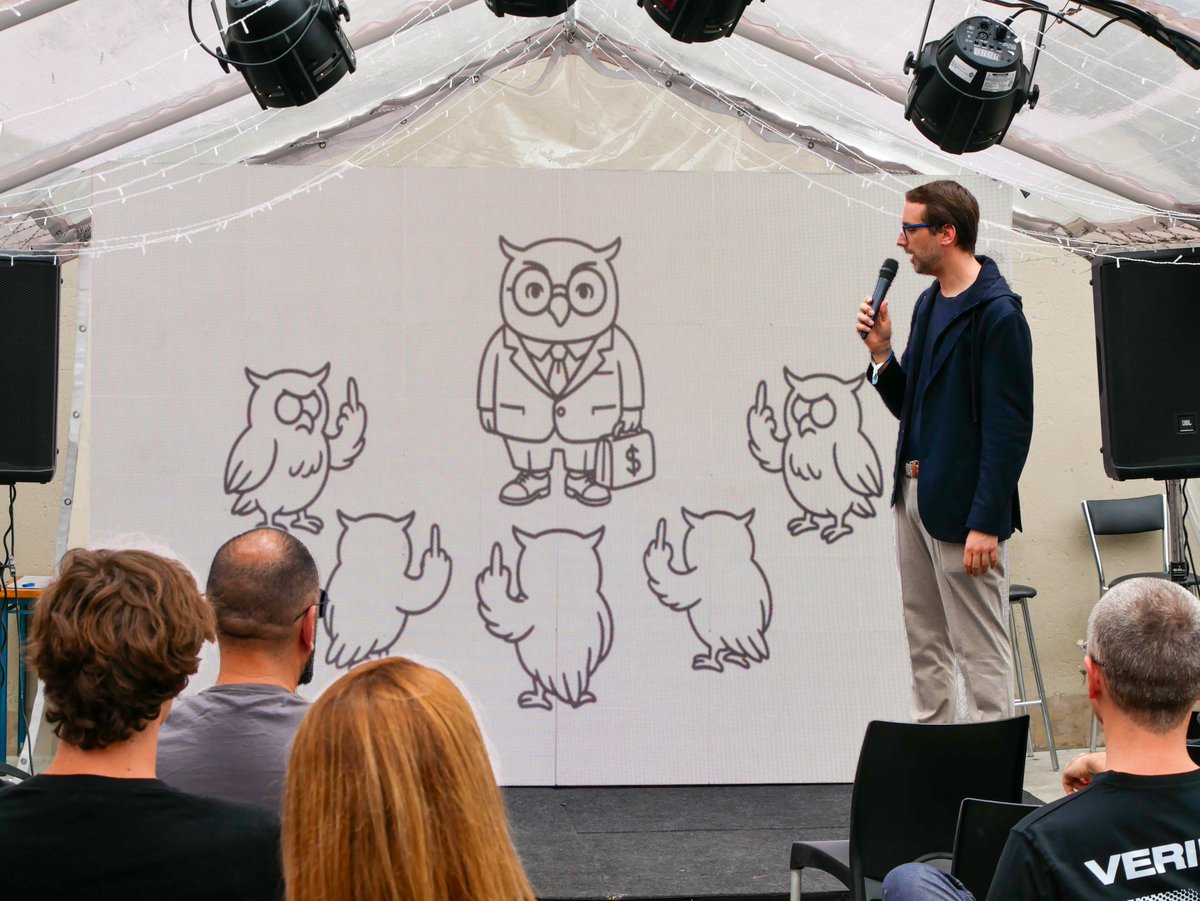 Sebastian Buergel 在 Cypherpunk 大会上发言，背景有朋克风格的猫头鹰竖中指插画