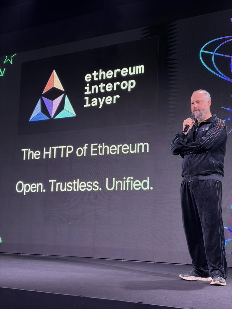 Speaker presenting Ethereum Interop Layer on stage with slogan 'The HTTP of Ethereum. Open. Trustless. Unified.'
