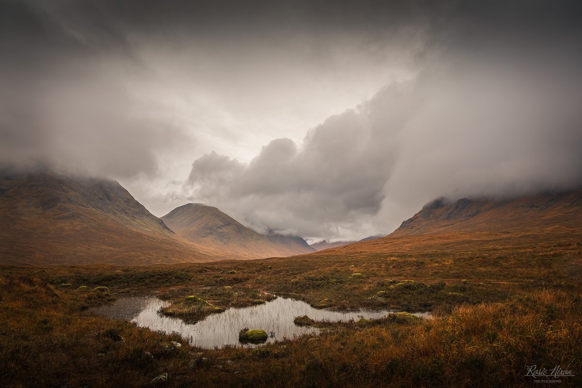 Heavy charcoal clouds roll over the rusty bracken mountains of Glen Etive. Then every few minutes a shaft of light slips through &amp; softly lights up one of the mountain slopes. While in the foreground the moss around the little lochan glows almost lime-green. #scotland