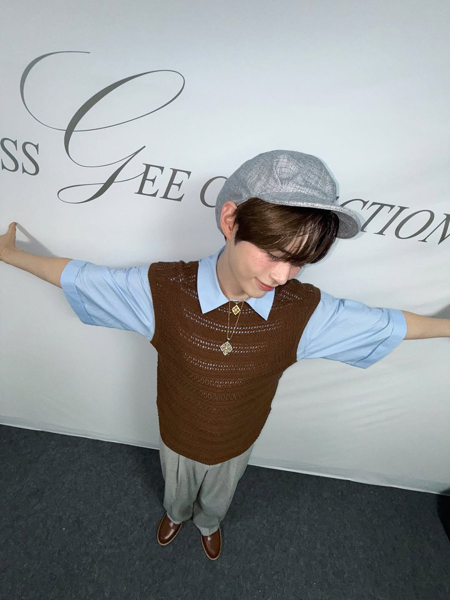 Hanbing's tweet image. Arms spread wide like I’m about to take flight! The overhead angle captures my pure joy as I stand before the elegant backdrop. My brown vest and grey trousers complete this vintage-inspired look, while my hat adds that perfect finishing touch to the whole ensemble.