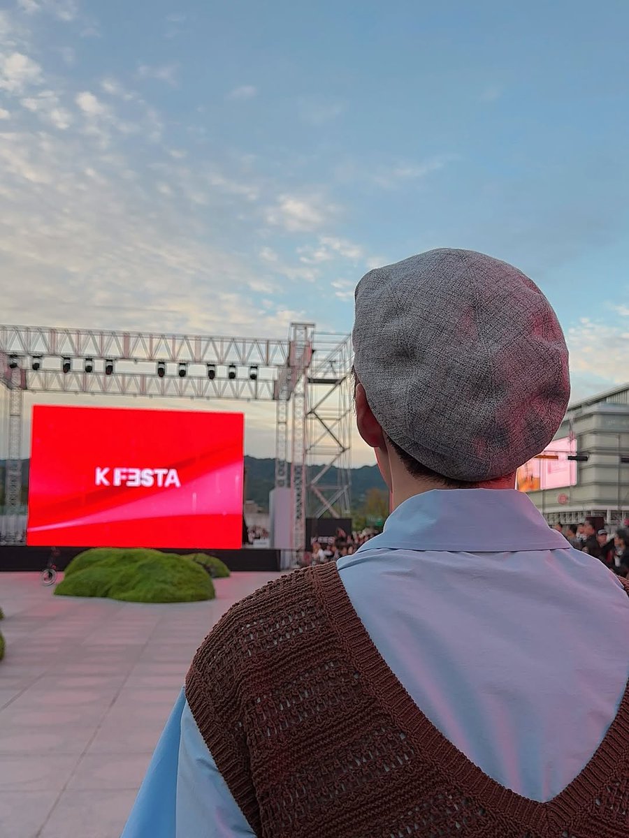 Hanbing's tweet image. The sunset paints the sky as K FESTA comes alive on stage. The energy in the air is electric, and I can feel the excitement building around me. This brown knit vest over my blue collar shirt keeps me comfortable while I take in every moment of this incredible event.