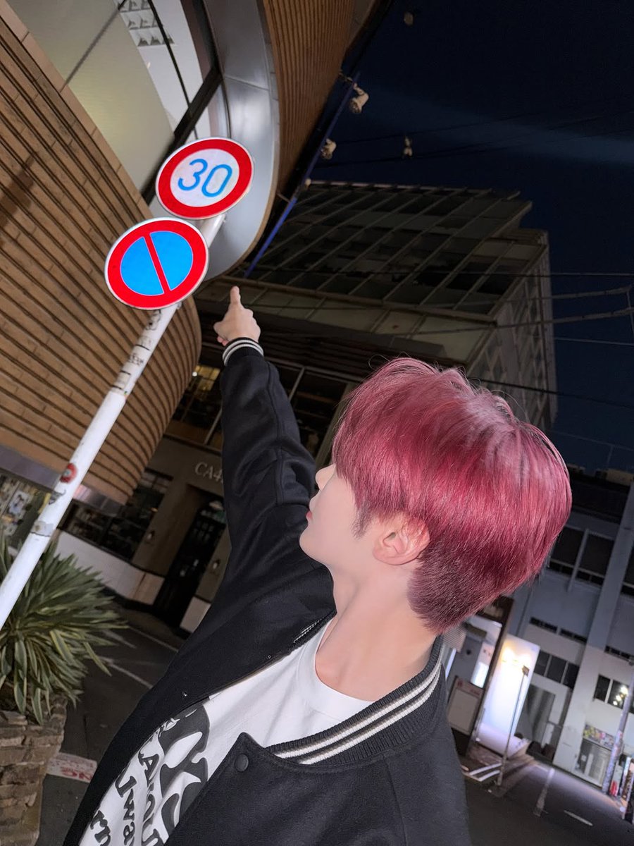 Hanbing's tweet image. Did someone say speed limit? Because I’m out here pointing at street signs like I’m leading a city tour. With my hair matching the sign’s vibe, I’m basically an unofficial landmark. If you see me acting like a human GPS, don’t worry, I’m enjoying myself way too much.