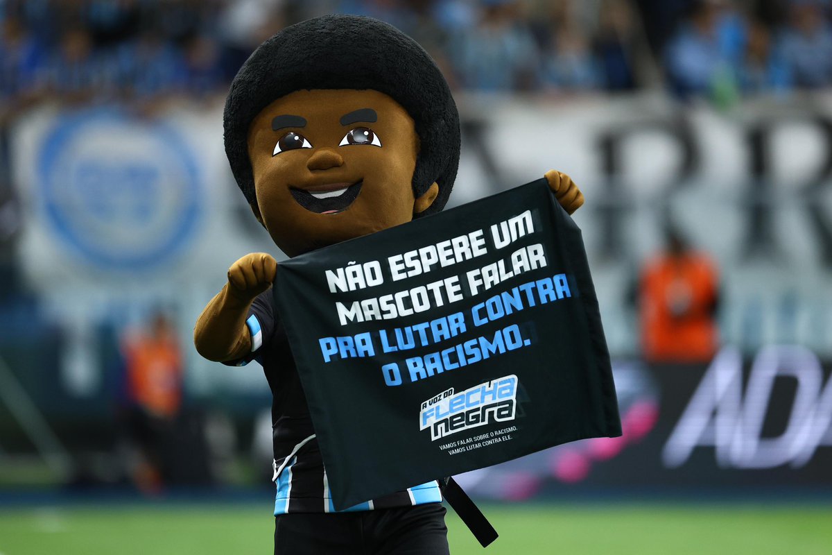 Gremio's tweet photo. ���𝐚𝐦𝐨𝐬 𝐟𝐚𝐥𝐚𝐫 𝐬𝐨𝐛𝐫𝐞 𝐨 𝐫𝐚𝐜𝐢𝐬𝐦𝐨. 𝐕𝐚𝐦𝐨𝐬 𝐥𝐮𝐭𝐚𝐫 𝐜𝐨𝐧𝐭𝐫𝐚 𝐞𝐥𝐞 🇪🇪✊🏿

O jogo desta noite marca o lançamento da campanha em alusão ao Dia da Consciência Negra. O mascote Flecha Negra é nossa voz na luta antirracista! 

📸 Lucas Uebel | Grêmio FBPA 

Detalhes em https://t.co/sTiDBRg9VQ