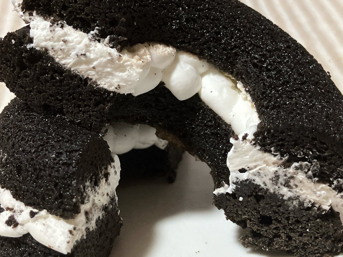 ローソン 黒い焼きドーナツサンド バニラクリーム。ショコラ生地はしっとりほろっと、甘くほんのりココアのビター感がありアーモンドの風味もしてフィナンシェのよう。クリームは甘くバニラが香りミルキー。合わせて食べるとクッキークリームのような味で、しっかり甘く食べごたえありおいしかった。