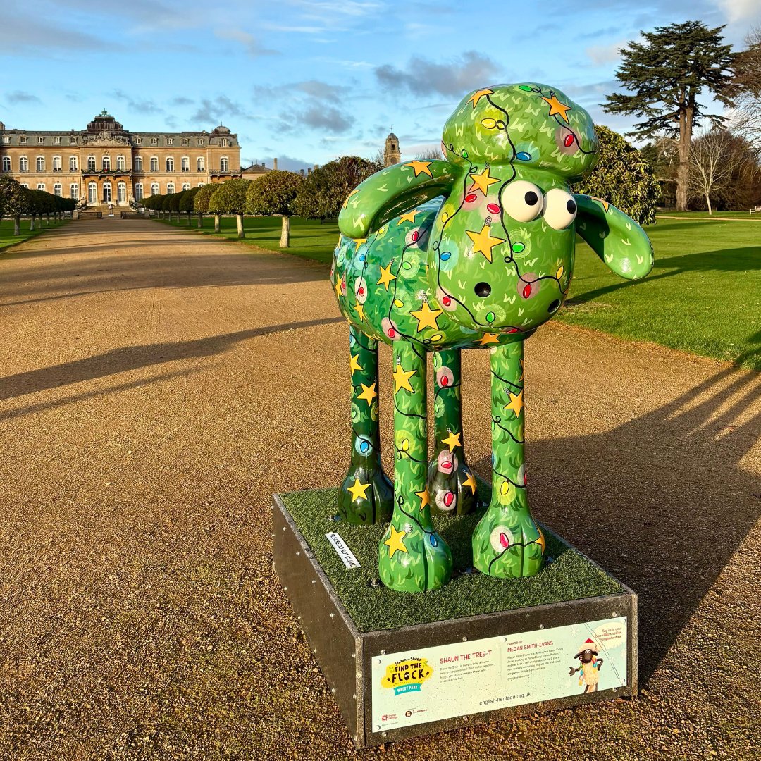 A colourful Shaun the Sheep sculpture stands on a path in front of a stately building. The sheep is green, decorated with stars and ornaments, evoking a playful and festive atmosphere.
