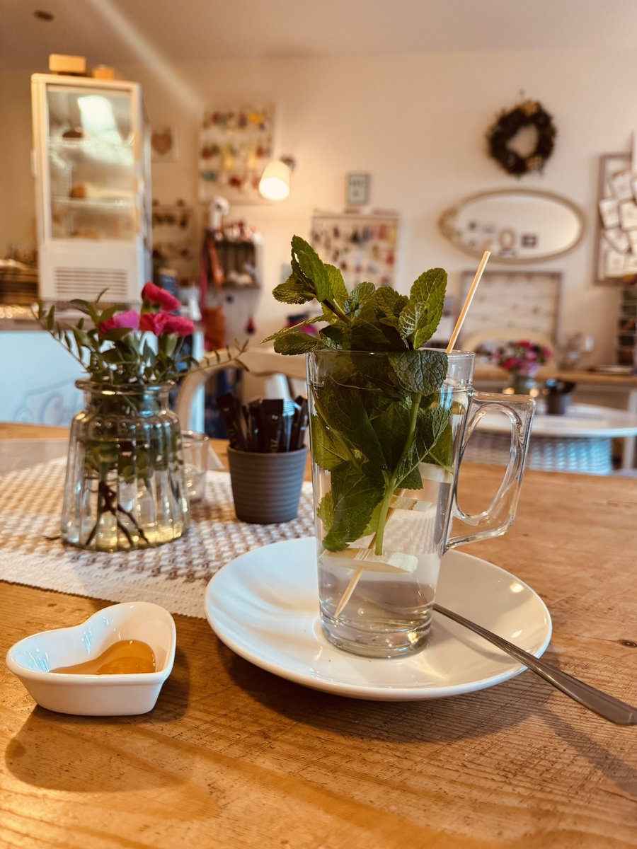 Wir sind heute beim Spaziergang zufällig in dieses kleine Wohnzimmer-Café gestolpert: Holzstühle mit weichen Sitzkissen, Regale voller Postkarten, kleine gehäkelte Figuren – und dazu ein Tee mit frischer Minze, Ingwer und einem Löffel Honig. Genau das Richtige für graue