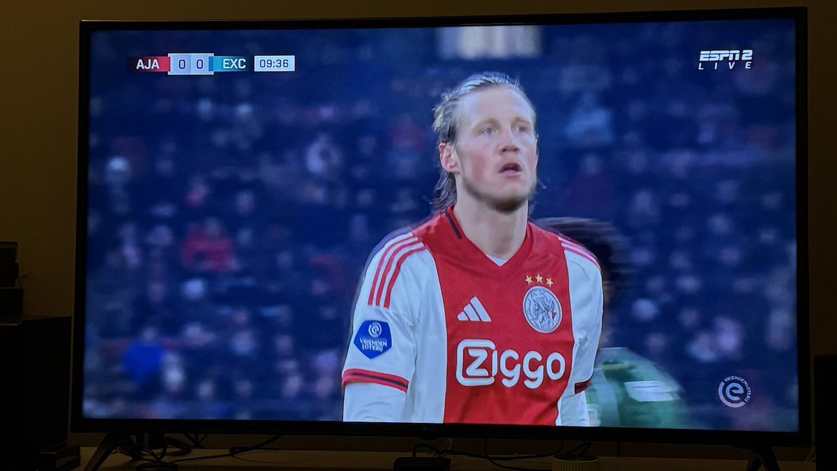 O Ajax vai jogar com o Benfica. 
A liga holandesa é transmitida em Portugal. 
Para se ver Eredivisie tem que se pagar. 
Mesmo pagando a esse operador, o jogo do Ajax não está a ser transmitido. 
Há maneiras alternativas de vermos o próximo adversário do Benfica e não pode ser