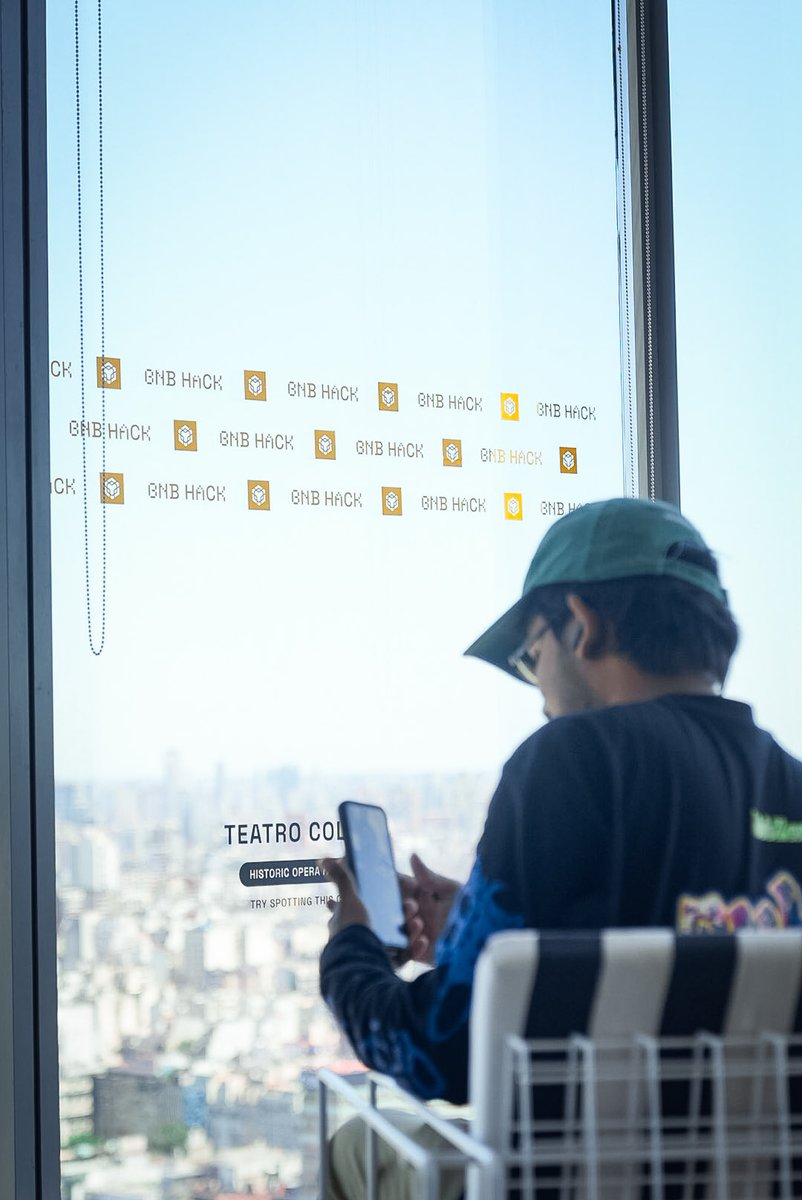 一人透过装饰有 BNB Hack 贴纸的窗户在科隆剧院眺望布宜诺斯艾利斯市景