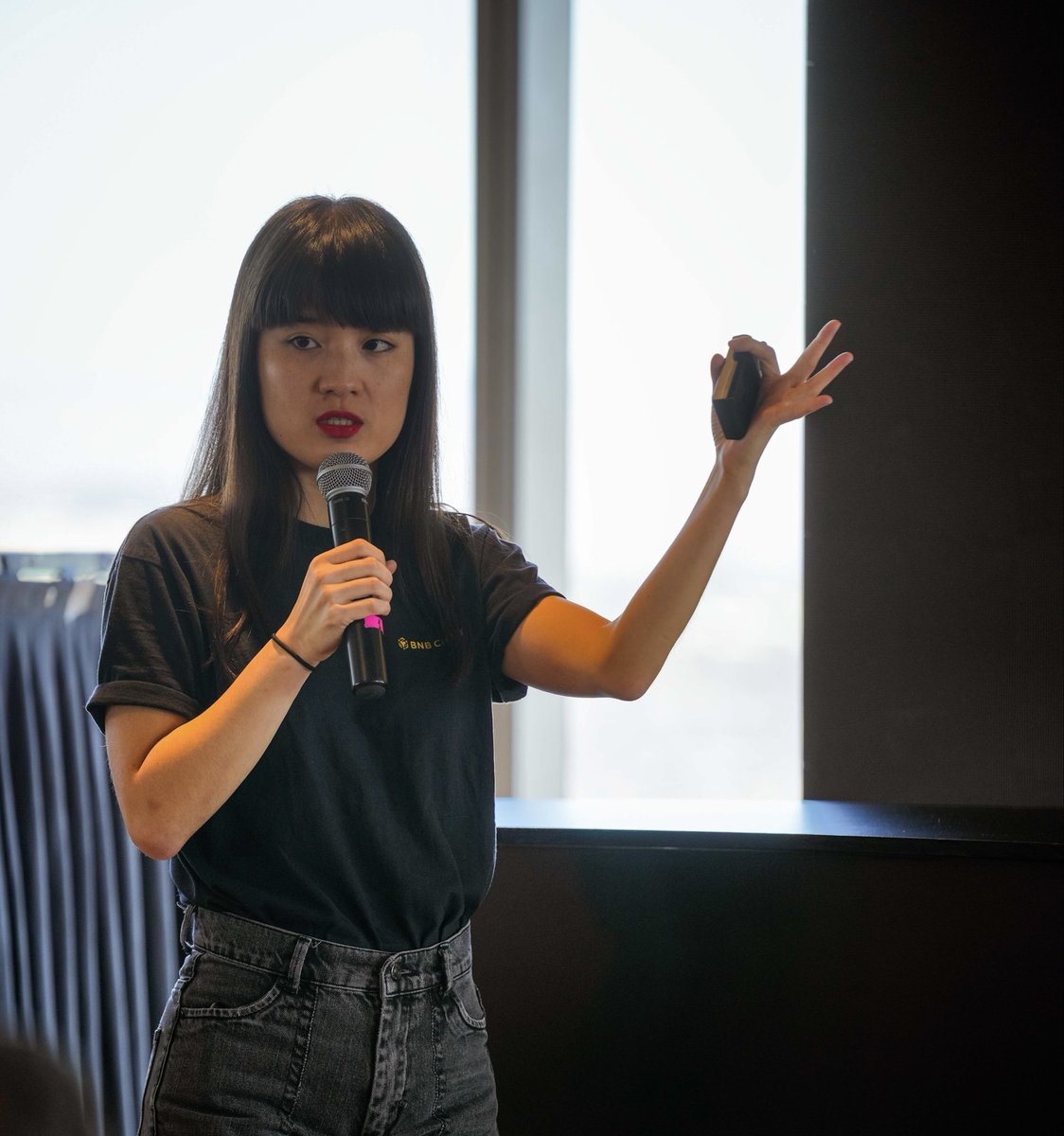 一名女性在 BNB Hack 活动中一边拿着物品一边对着麦克风发言